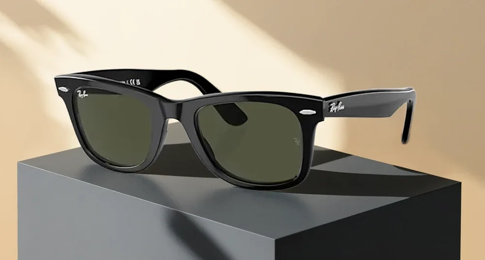 Dark sunglasses on a charcoal plinth with warm light and diagonal shadows.